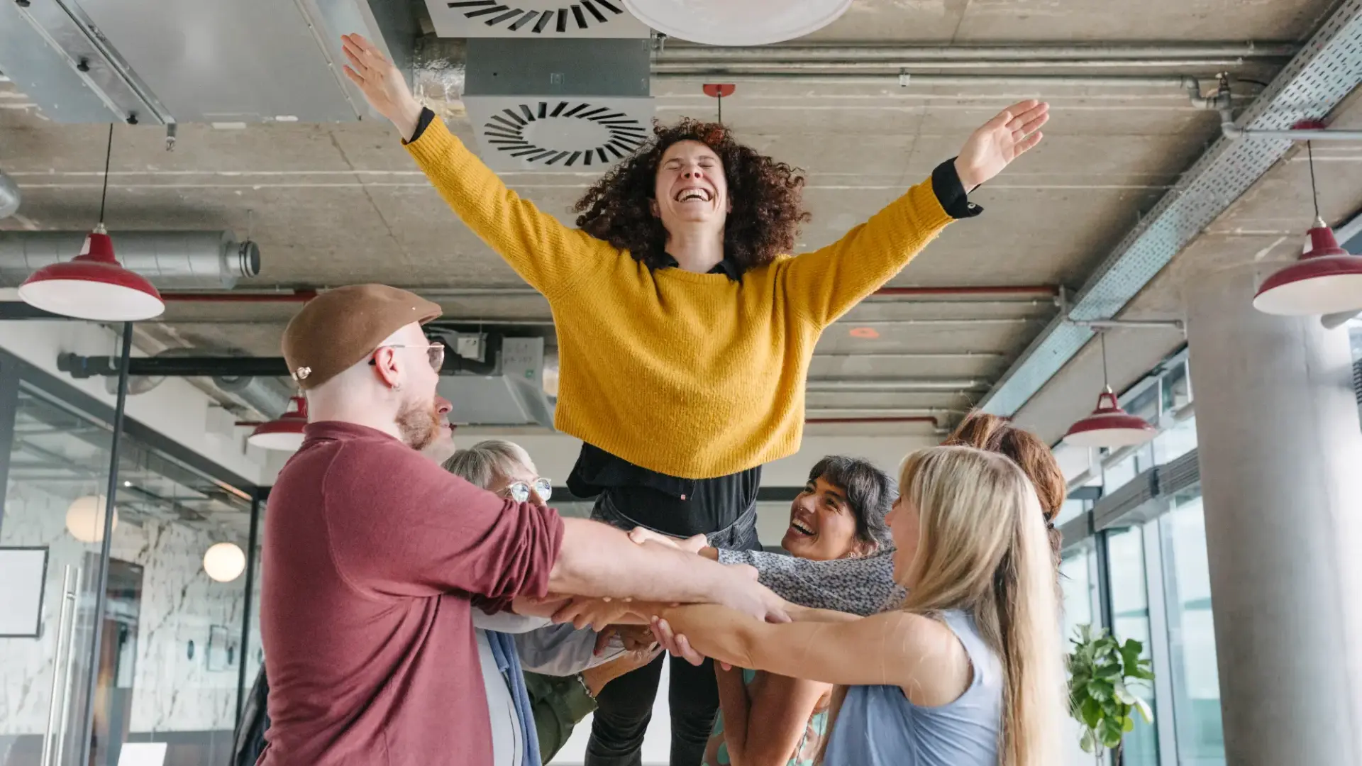 A group of office colleagues taking part in a bonding exercise, catching a woman as she closes her eyes and falls into her coworkers arms in a trust fall.